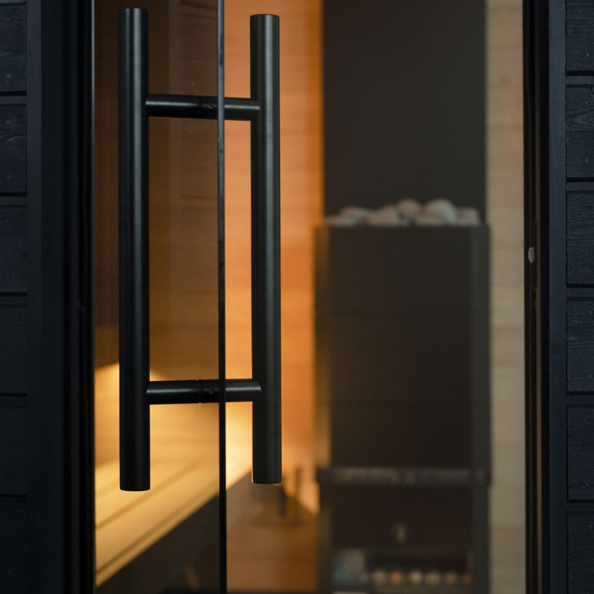 Black handle and glass door of a SaunaLife G6 sauna, with warmly lit wood inside.